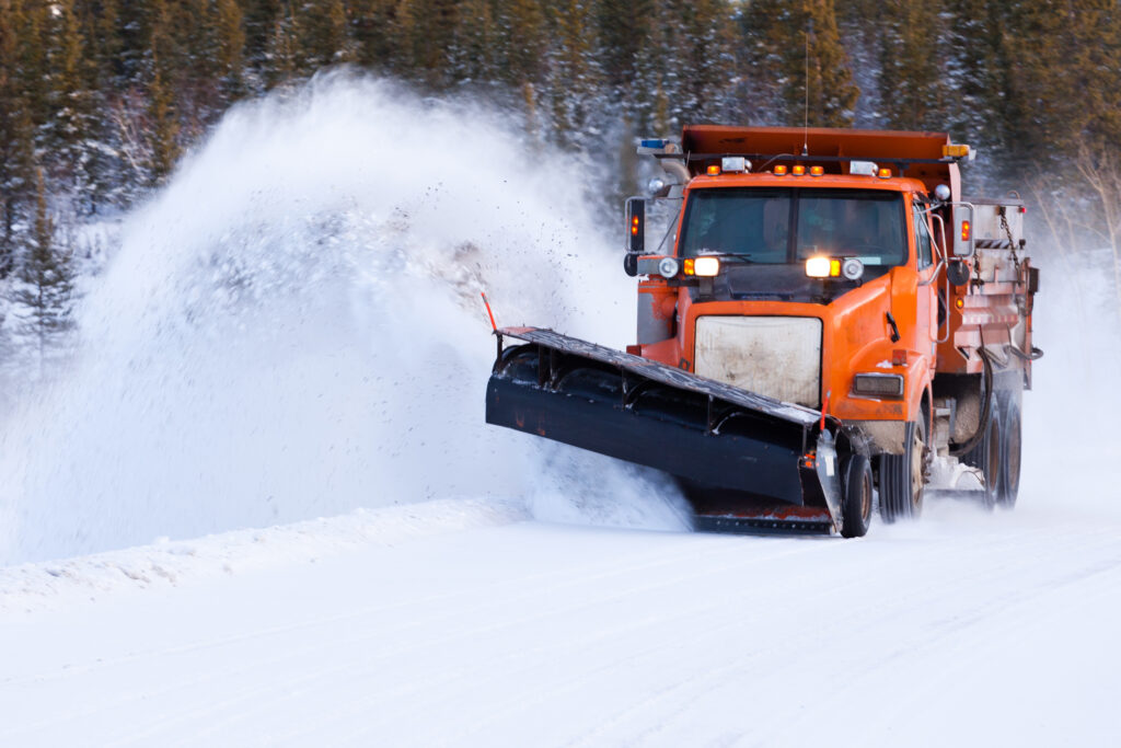 a snow plow clearing the road in front of some trees